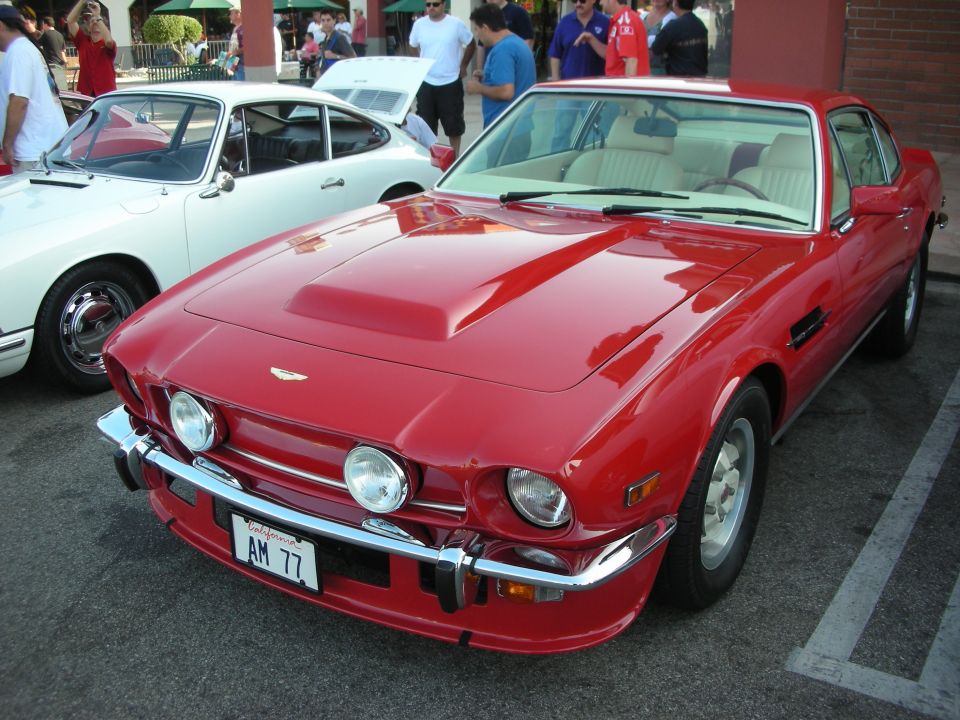 Red coupe with a hood scoop and chrome bumper, parked next to a white car