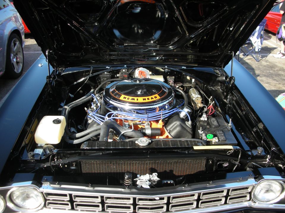 Engine bay of a classic car with a Hemi Head air cleaner and blue spark plug wires. Another car is visible to the left