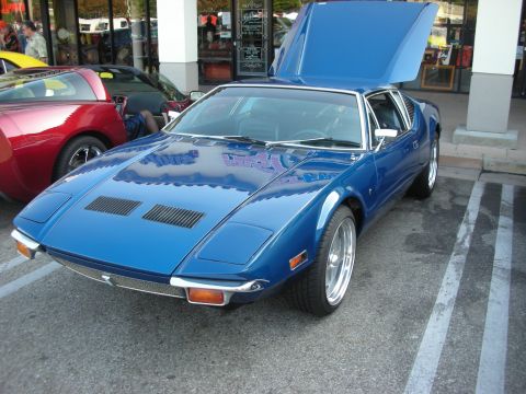 1998 Ford Crown Victoria - A blue De Tomaso Pantera is parked in a lot with its hood open, alongside other vehicles.