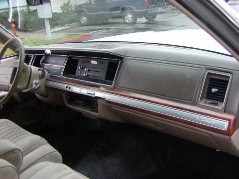1991 Ford LTD Crown Victoria - Dashboard of a gray-interior Ford shot from the passenger side, showing the woodgrain trim strip with 'LTD Crown Victoria' badge on the glo…