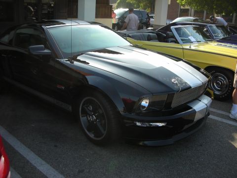 1998 Ford Crown Victoria - A black Ford Mustang with racing stripes is parked at an outdoor car meet.