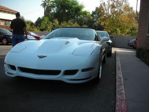 1998 Ford Crown Victoria - A white Chevrolet Corvette is parked in a lot, facing forward. Another vehicle is parked behind it.