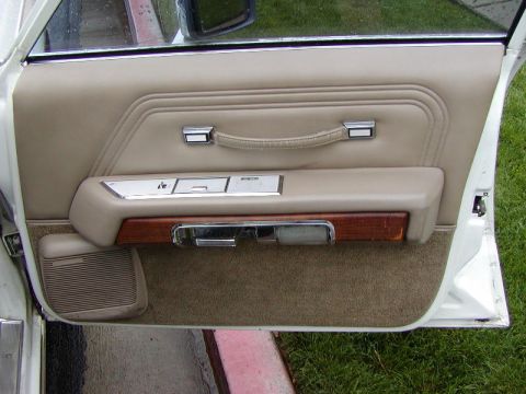 1991 Ford LTD Crown Victoria - Interior of an open driver's door on a white Ford sedan, showing the tan vinyl door panel with a stitched pull strap, chrome-trimmed power…