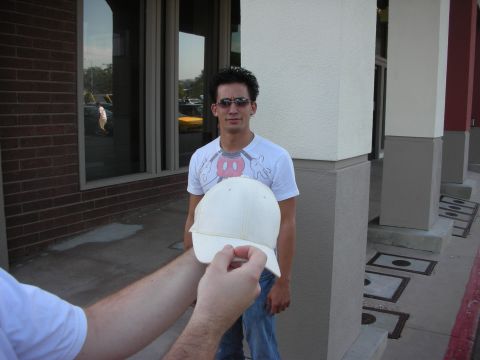 1998 Ford Crown Victoria - A man wearing a Mickey Mouse t-shirt stands outside a building while another person holds a baseball cap in front of him.