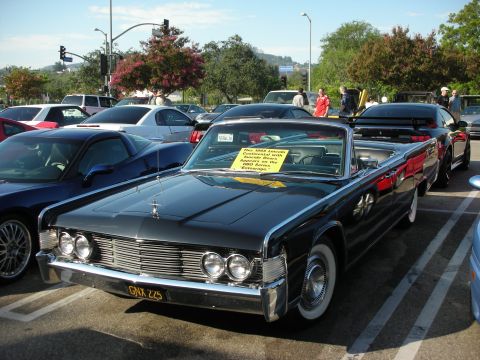 1998 Ford Crown Victoria - A classic black Lincoln Continental convertible is parked in a lot with other vehicles, displaying a sign with information about the car.