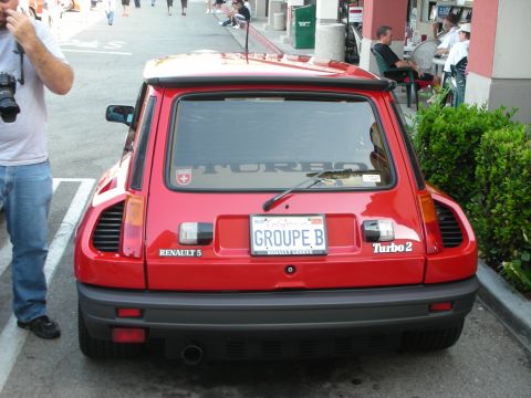 1998 Ford Crown Victoria - A red Renault 5 Turbo 2 is parked, displaying its rear with a custom 'GROUPE B' license plate.