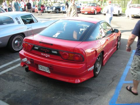 1998 Ford Crown Victoria - A red Nissan 240SX is parked in a lot with other vehicles and people milling around.