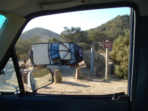 1985 Toyota Hilux - Vehicle overturned on rocks with a 'Squeeze Rock' sign nearby.