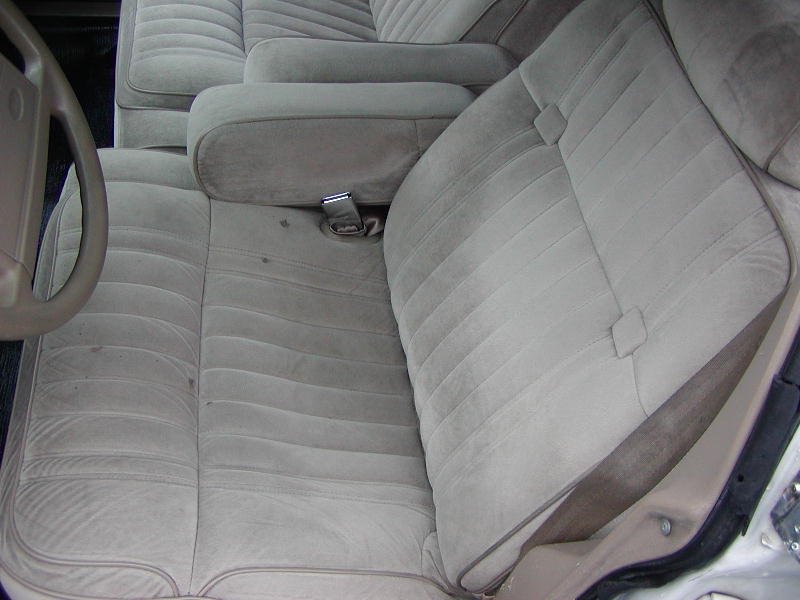 Car interior with light gray velour seats and armrests, showing part of the steering wheel