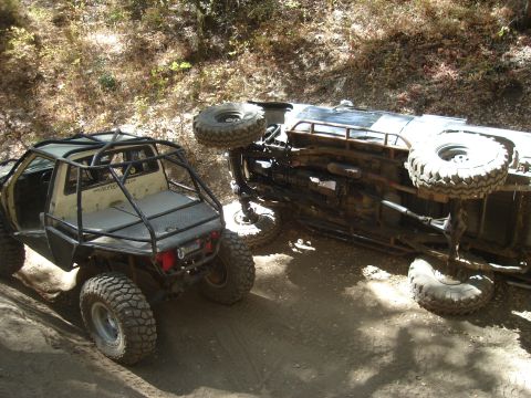 1985 Toyota Hilux - Two heavily modified off-road trucks are shown on a dirt path, with one vehicle overturned.