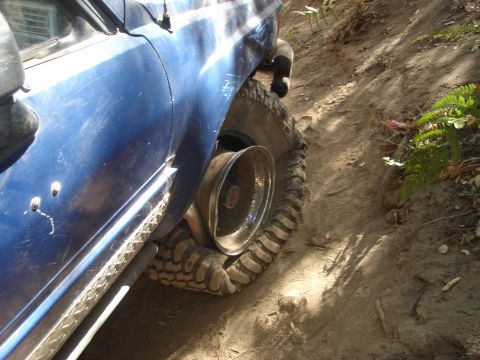 1985 Toyota Hilux - Vehicle with a flat tire on a dirt trail, rim exposed.