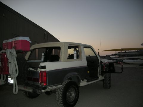 1991 Ford Bronco - A two-tone Ford Bronco is parked outside a building with aircraft in the background at dusk.