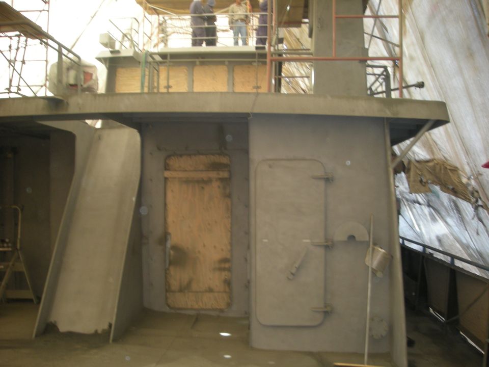 Ship interior under construction with plywood-covered door and metal hatch
