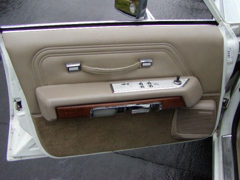 1991 Ford LTD Crown Victoria - Open driver's door of a white Ford sedan showing the tan vinyl door panel: stitched pull strap, chrome switch plate with four power-window…