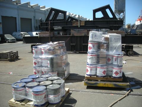 1991 Ford Bronco - Two pallets of paint cans are shrink-wrapped and stacked in an outdoor industrial setting with large metal structures in the background.