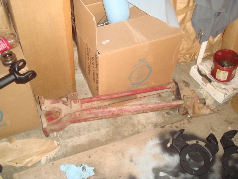1992 Ford Bronco - A pair of red-painted radius arms and a steering/track bar assembly with knuckle ends lying on a garage floor next to cardboard boxes, with…