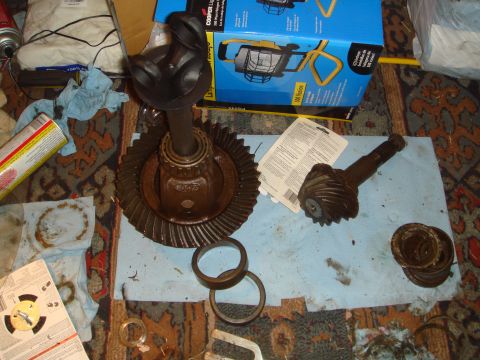 1992 Ford Bronco - Disassembled differential parts laid out on a blue shop towel over a rug: a rusty ring gear bolted to a carrier with an axle shaft standing…
