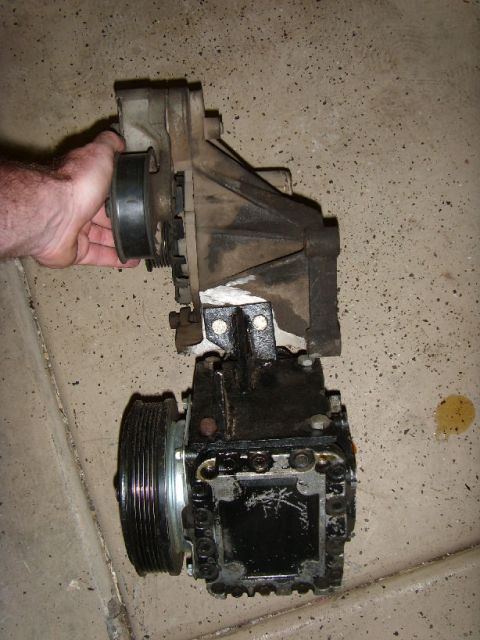 1989 Ford F-250 - AC compressor and bracket removed from a vehicle, placed on a concrete surface.