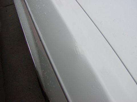 1991 Ford LTD Crown Victoria - Extreme close-up along the wet white bodyside of a car, looking down the fender/hood edge and chrome drip trim, with a small paint blemish…