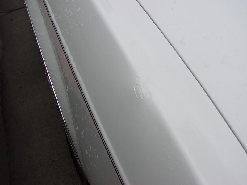Close-up of a wet white car body panel and chrome trim showing a small paint blemish