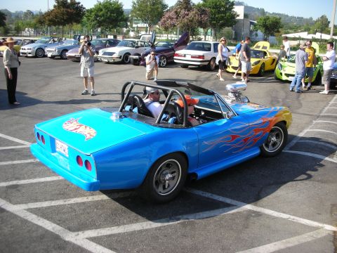 1998 Ford Crown Victoria - A custom blue convertible with flame decals and a prominent Hot Wheels logo is parked among other vehicles at an outdoor gathering.