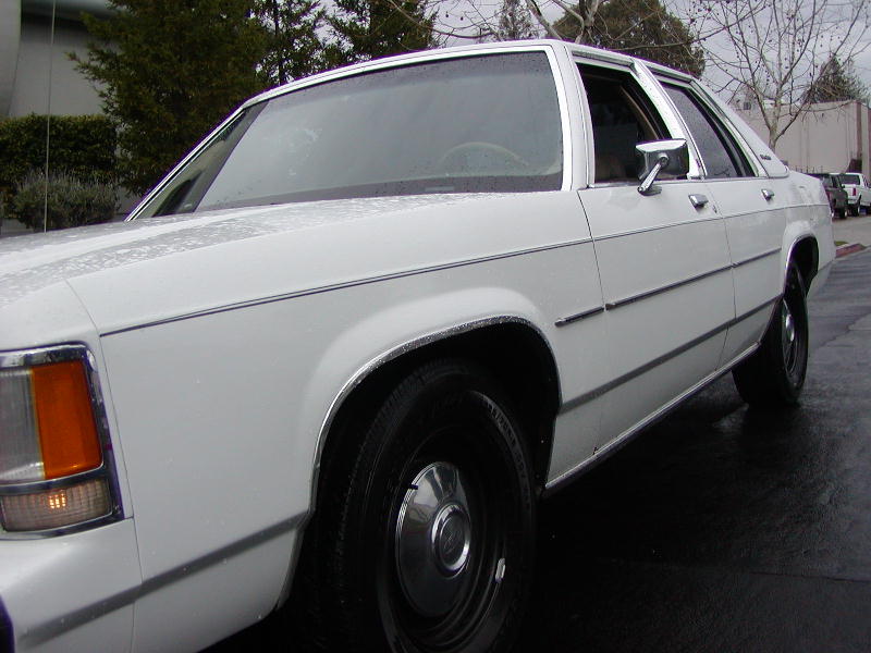 Close low side view of white Ford Crown Victoria front fender, wheel and chrome trim