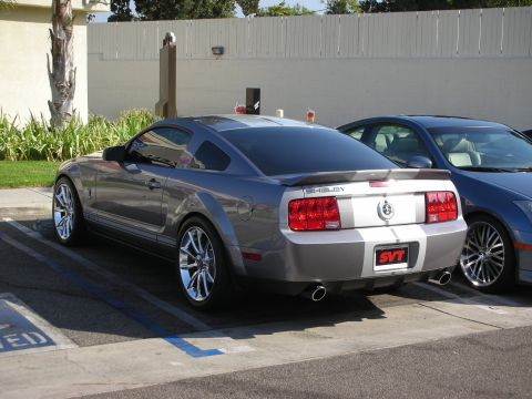 1998 Ford Crown Victoria - A gray Ford Mustang Shelby GT500 is parked next to another car, showing its rear end with racing stripes and an SVT badge.