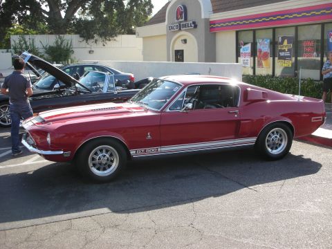 1998 Ford Crown Victoria - A red 1968 Ford Mustang Shelby GT500 is parked outside a Taco Bell, with another car's hood open in the background.
