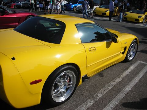 1998 Ford Crown Victoria - A bright yellow sports car is parked on a street, with other vehicles and people in the background.