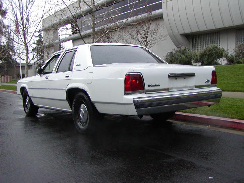White Ford LTD Crown Victoria sedan rear 3/4 view on a wet street