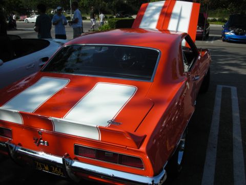 1998 Ford Crown Victoria - A classic orange Camaro with racing stripes is parked at an outdoor gathering with other vehicles and people.