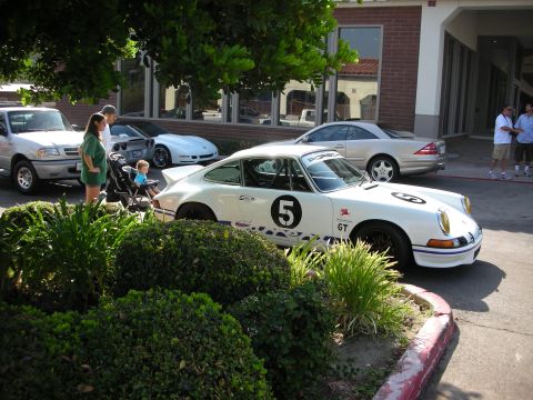 1998 Ford Crown Victoria - A white Porsche 911 with racing decals is parked next to other vehicles at a car meet.