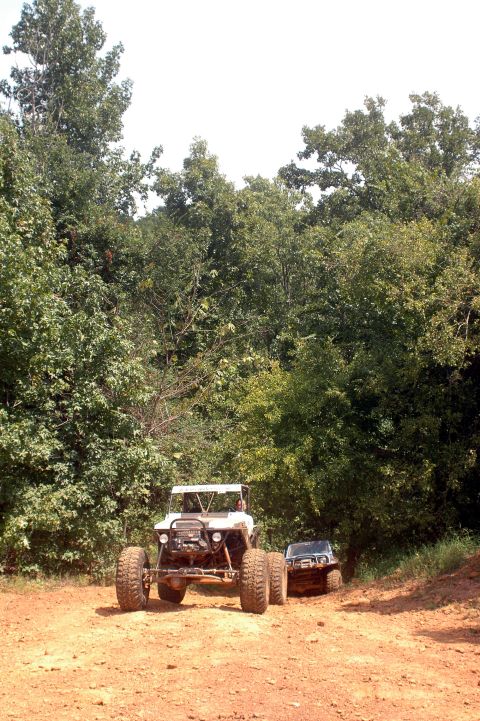 1987 Suzuki Samurai - Two off-road vehicles navigate a dirt trail through a wooded area.