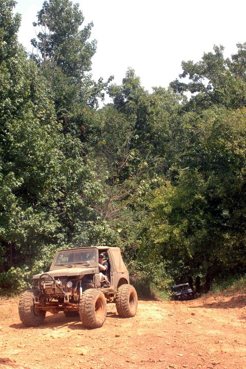 1987 Suzuki Samurai - A heavily modified off-road vehicle is parked on a dirt path with trees in the background. Another vehicle is visible further down the path.