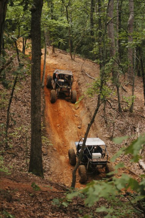 1987 Suzuki Samurai - Two buggies navigate a challenging dirt path through a dense wooded area.