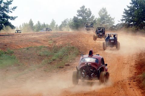 1987 Suzuki Samurai - Several off-road vehicles navigate a dusty trail through a wooded area.