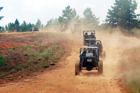 1987 Suzuki Samurai - A convoy of off-road vehicles navigates a dusty path, kicking up clouds of dirt.