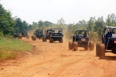 1987 Suzuki Samurai - A group of off-road vehicles travels down a dirt path, kicking up dust.