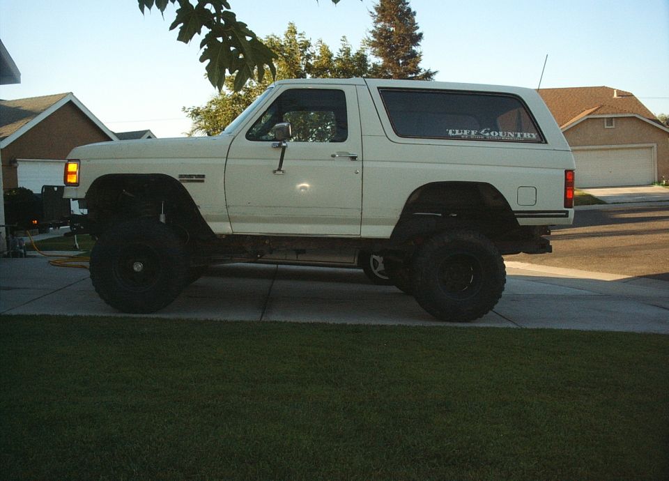 White 1987 Ford Bronco with lifted suspension and off-road tires parked in a driveway