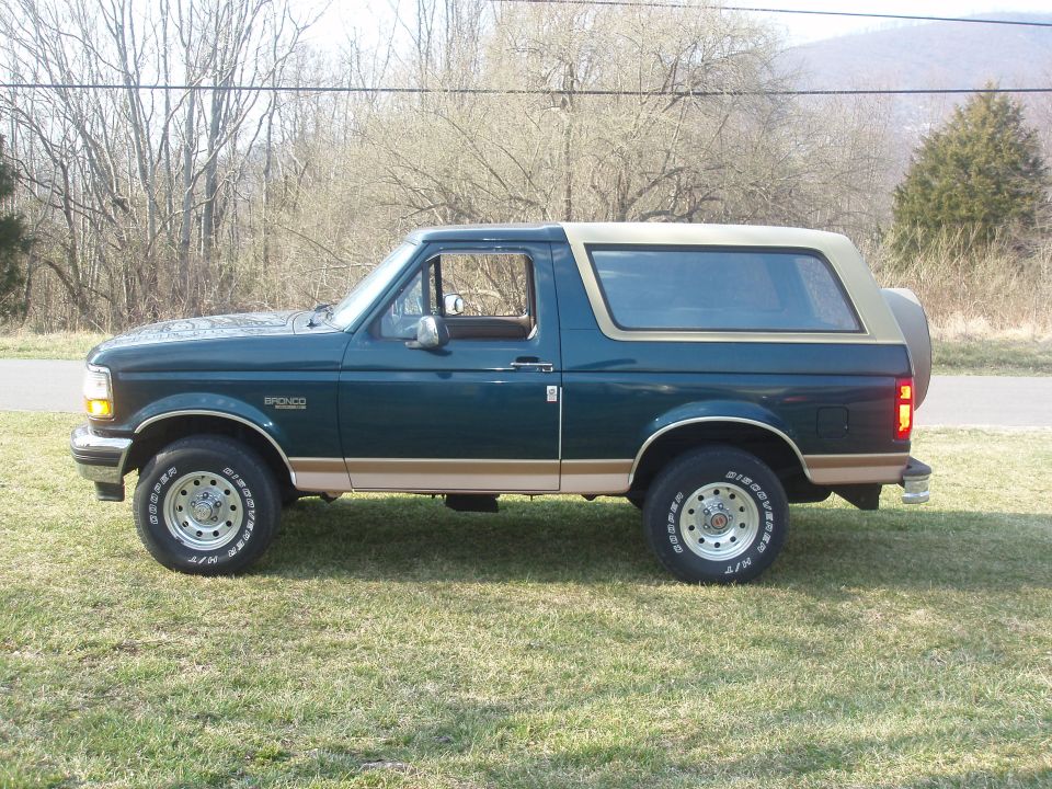 Dark green and tan Ford Bronco SUV, driver-side profile, parked on grass