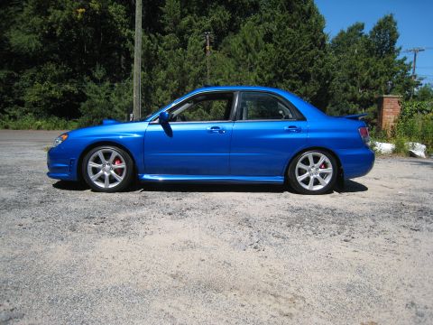 2007 Subaru Impreza - A blue Subaru sedan is shown from the side, parked on a gravel surface with trees in the background.