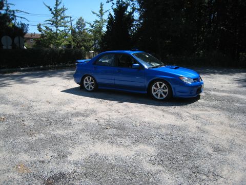 2007 Subaru Impreza - A blue 2007 Subaru Impreza WRX STI sedan is parked on a gravel surface under a clear sky.