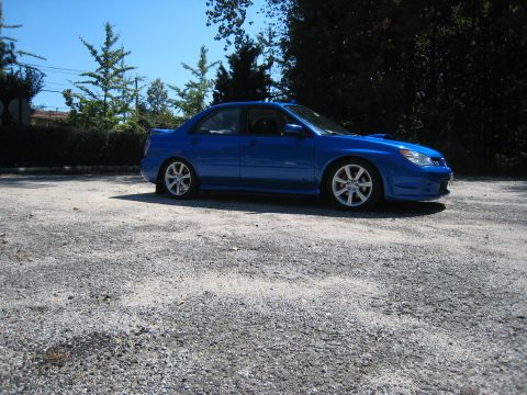2007 Subaru Impreza - A blue Subaru Impreza WRX sedan is parked on a gravel surface with trees and a clear blue sky in the background.