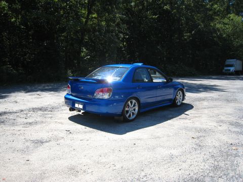 2007 Subaru Impreza - A blue Subaru Impreza sedan is parked on a gravel lot with trees in the background.