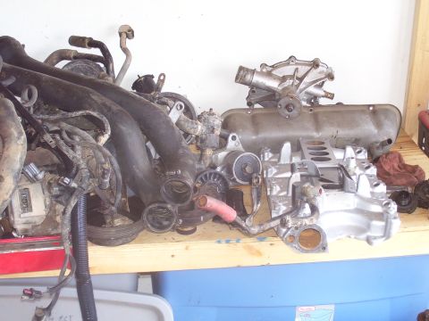 1991 Ford Bronco - Various engine components are laid out on a shelf, including an intake manifold, valve cover, and water pump.