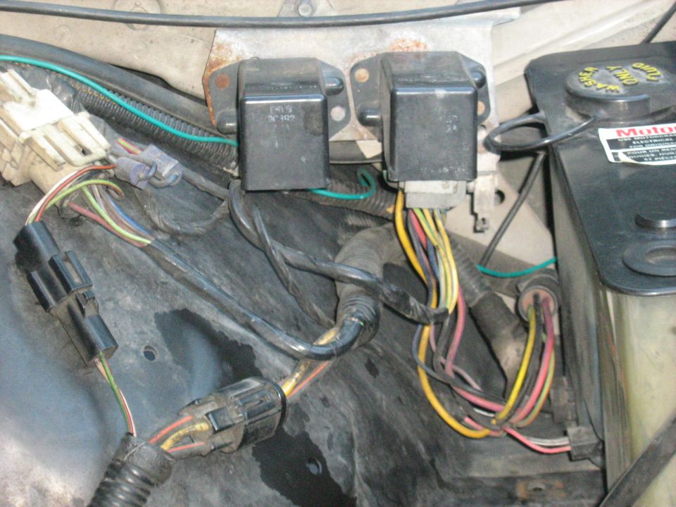 Engine compartment wiring with two black relays and a black plastic fluid reservoir with a yellow cap