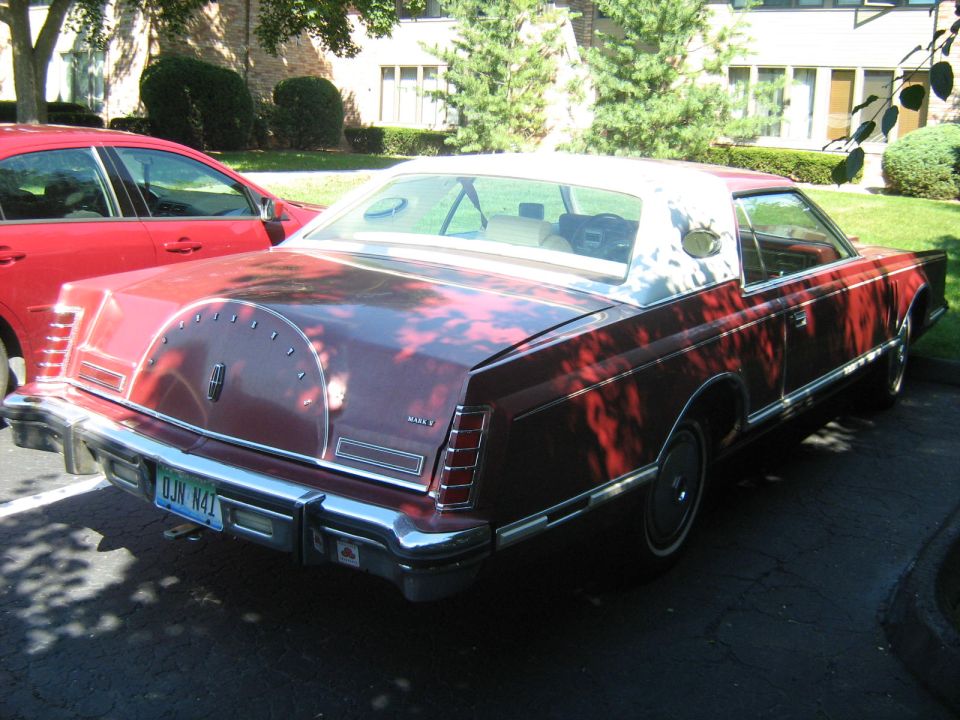 Red Lincoln Continental Mark V with a white vinyl roof and a continental kit on the trunk