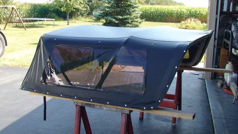 1979 Ford Bronco - A black soft top with clear windows is displayed on sawhorses, with a cornfield and trees in the background.