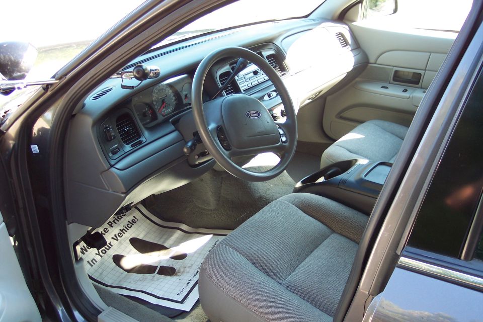2001 Ford Crown Victoria interior showing dashboard, steering wheel, and front seats. Floor mat reads 'We Make Pride In Your Vehicle!'