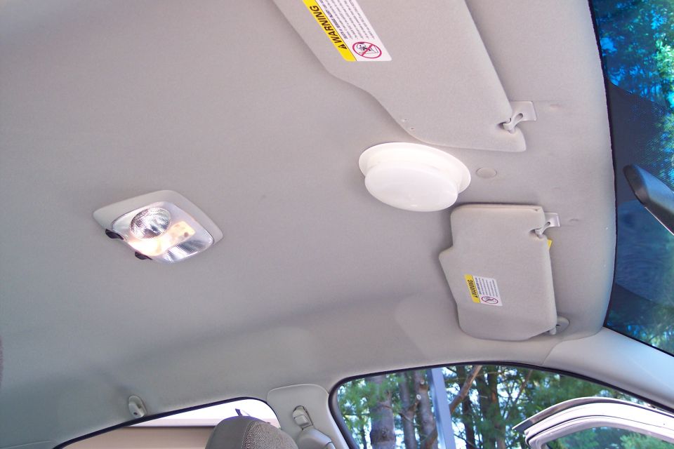Interior ceiling of a car showing two dome lights and two sun visors with warning labels
